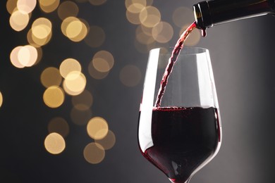 Pouring red wine into glass against grey background, closeup. Bokeh effect