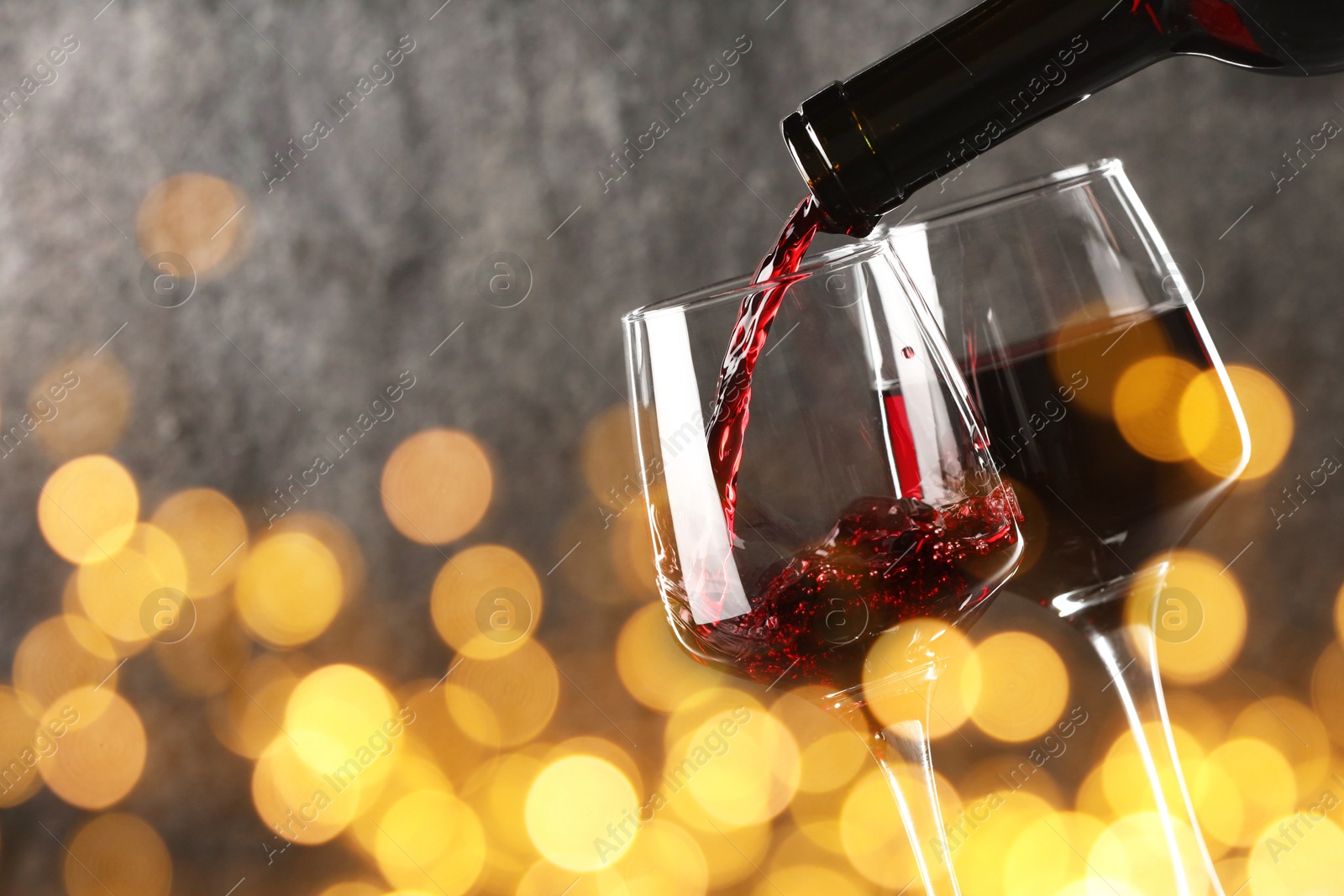 Image of Pouring red wine into glass against grey background, closeup. Bokeh effect