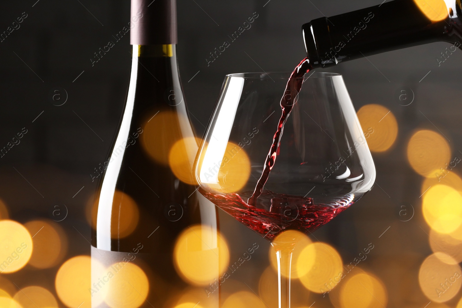 Image of Pouring red wine into glass against brick wall, closeup. Bokeh effect