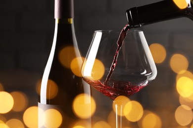 Pouring red wine into glass against brick wall, closeup. Bokeh effect