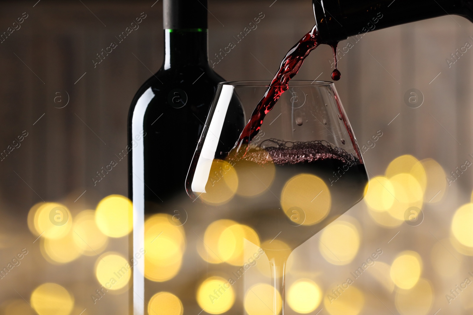 Image of Pouring red wine into glass against blurred background, closeup. Bokeh effect