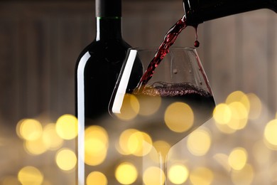 Pouring red wine into glass against blurred background, closeup. Bokeh effect