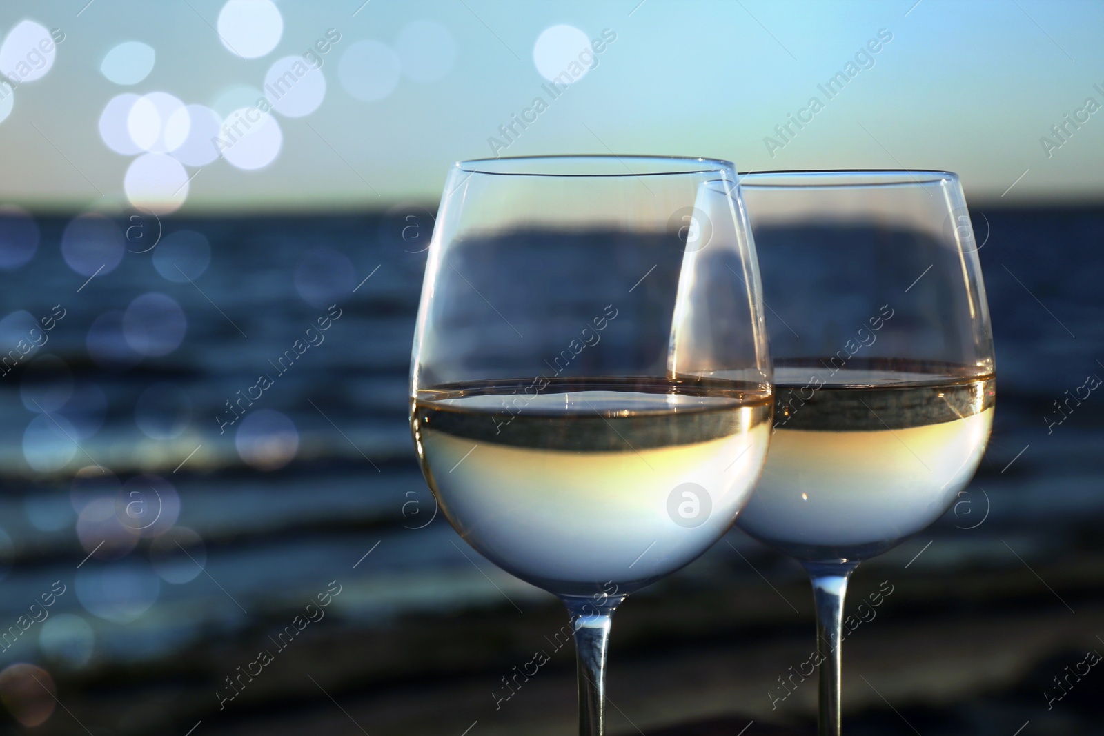 Image of Two glasses of wine near river at sunset, closeup. Bokeh effect