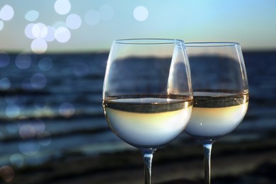 Two glasses of wine near river at sunset, closeup. Bokeh effect