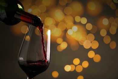 Pouring red wine into glass against blurred lights, closeup. Bokeh effect