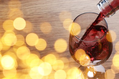 Pouring red wine into glass on table, closeup. Bokeh effect