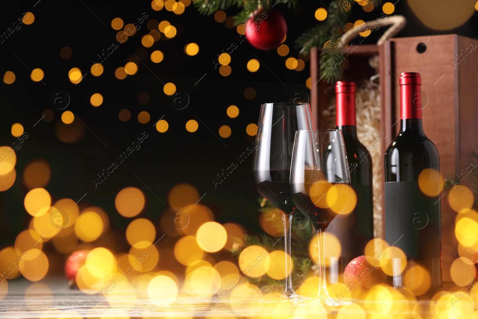 Image of Bottles of wine, glasses, wooden boxes, fir twigs and red Christmas balls on table, space for text. Bokeh effect