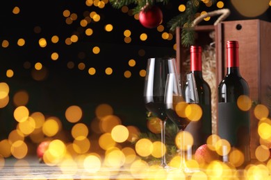 Bottles of wine, glasses, wooden boxes, fir twigs and red Christmas balls on table, space for text. Bokeh effect