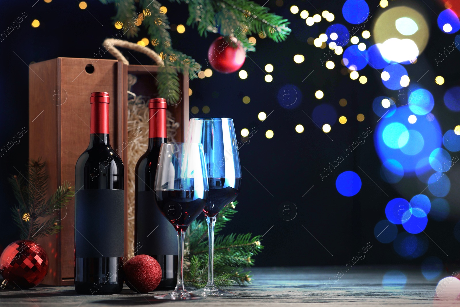 Image of Bottles of wine, glasses, wooden boxes, fir twigs and red Christmas balls on table, space for text. Bokeh effect