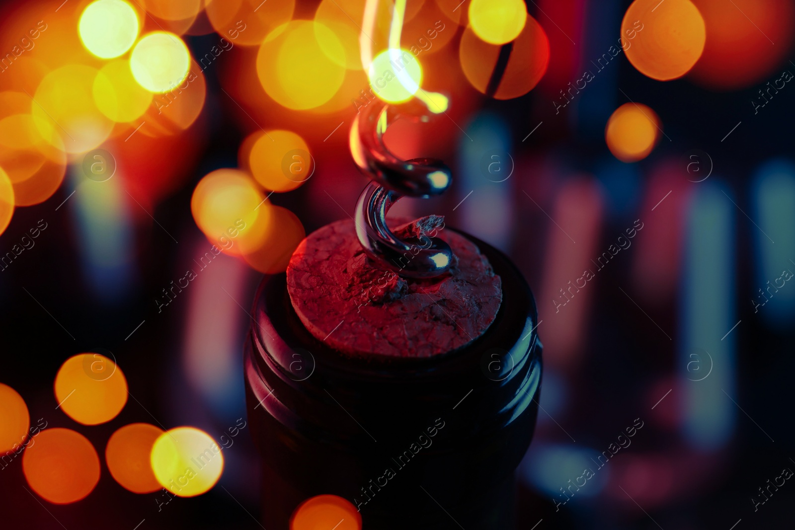 Image of Opening wine bottle with corkscrew on blurred background, closeup. Bokeh effect