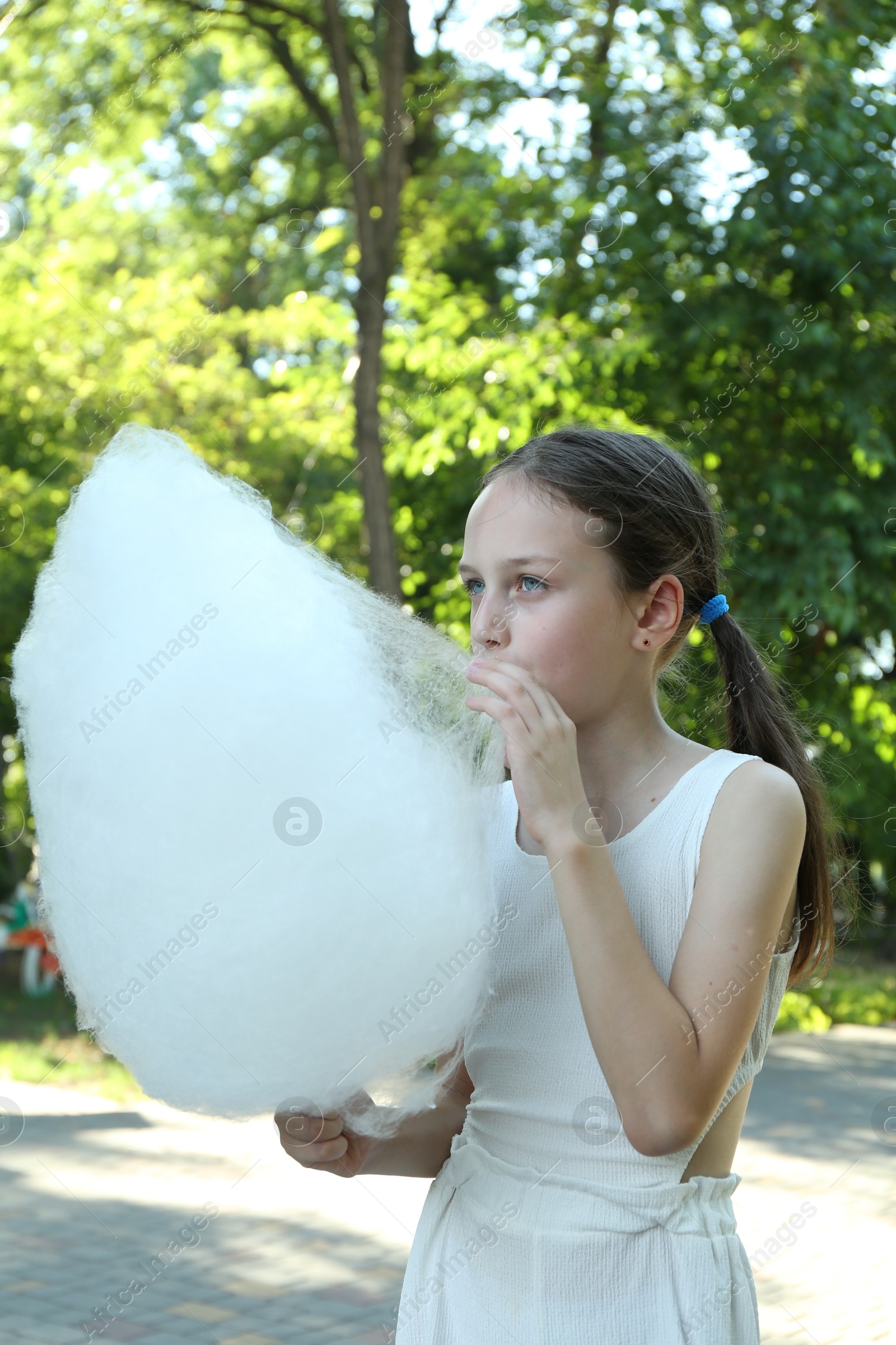 Photo of Little girl eating sweet cotton candy in park