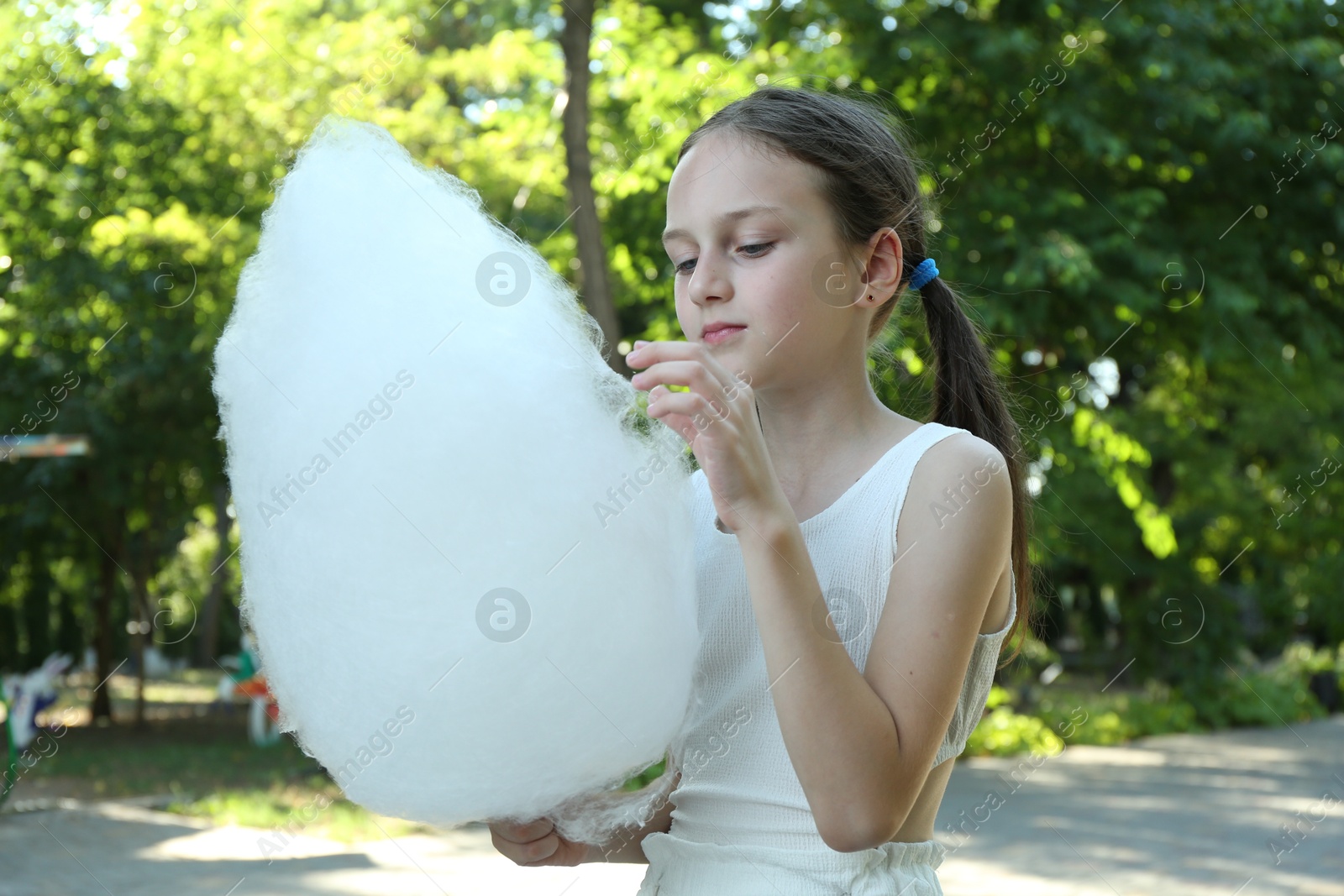 Photo of Little girl eating sweet cotton candy in park