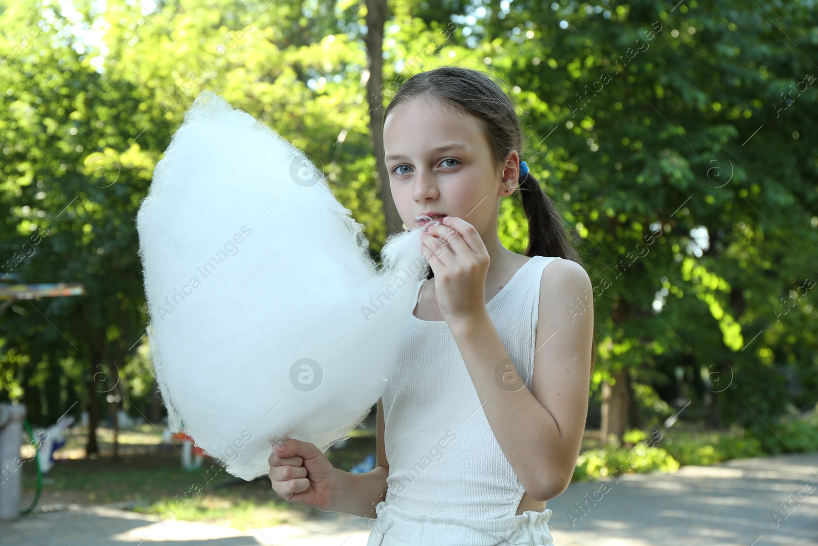 Photo of Little girl eating sweet cotton candy in park