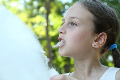 Photo of Little girl eating sweet cotton candy in park, closeup