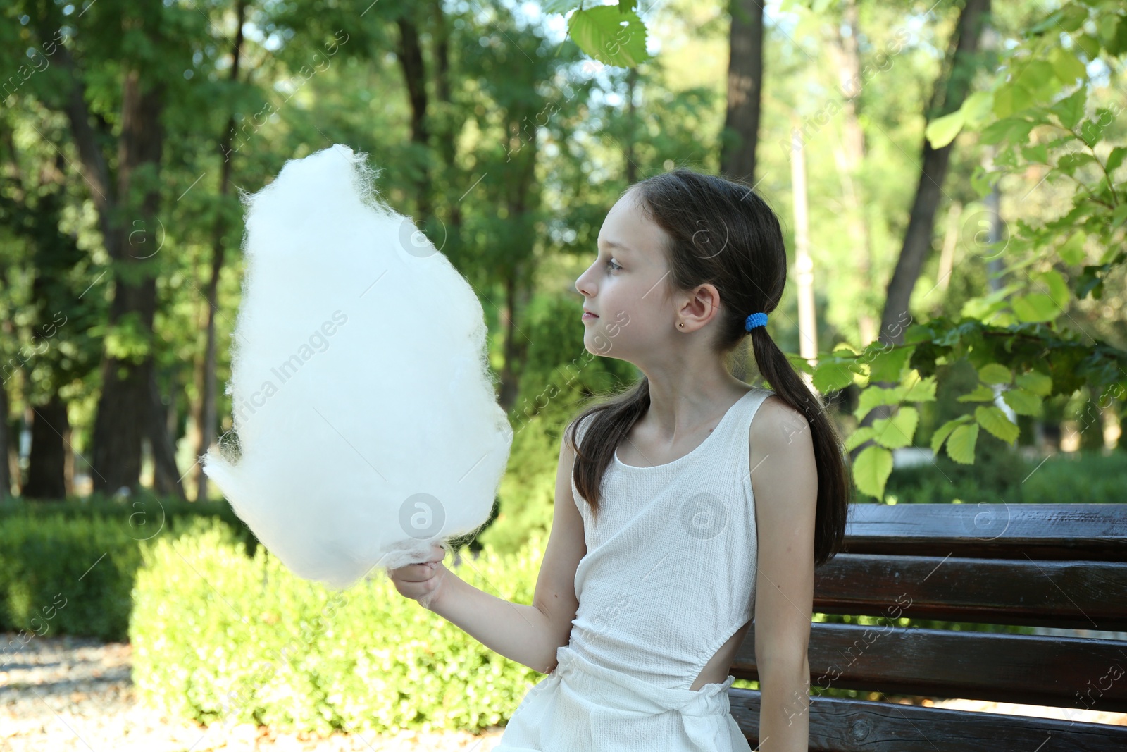 Photo of Portrait of little girl with sweet cotton candy on bench in park