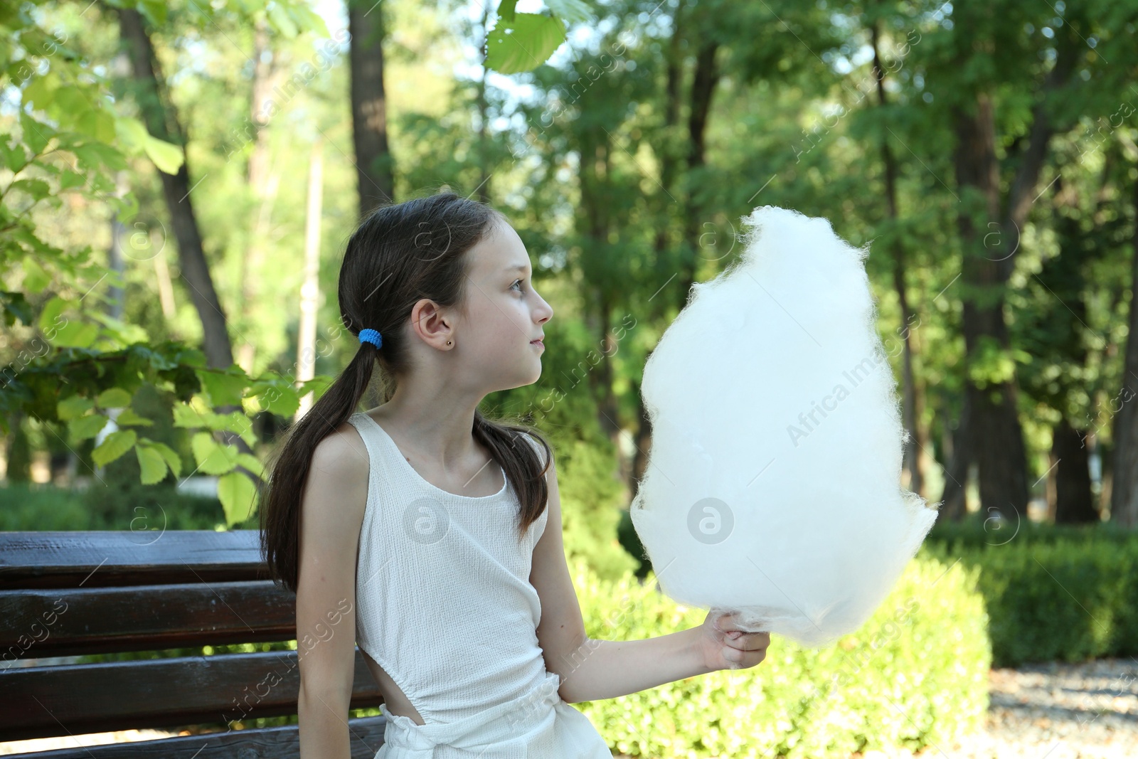 Photo of Portrait of little girl with sweet cotton candy on bench in park