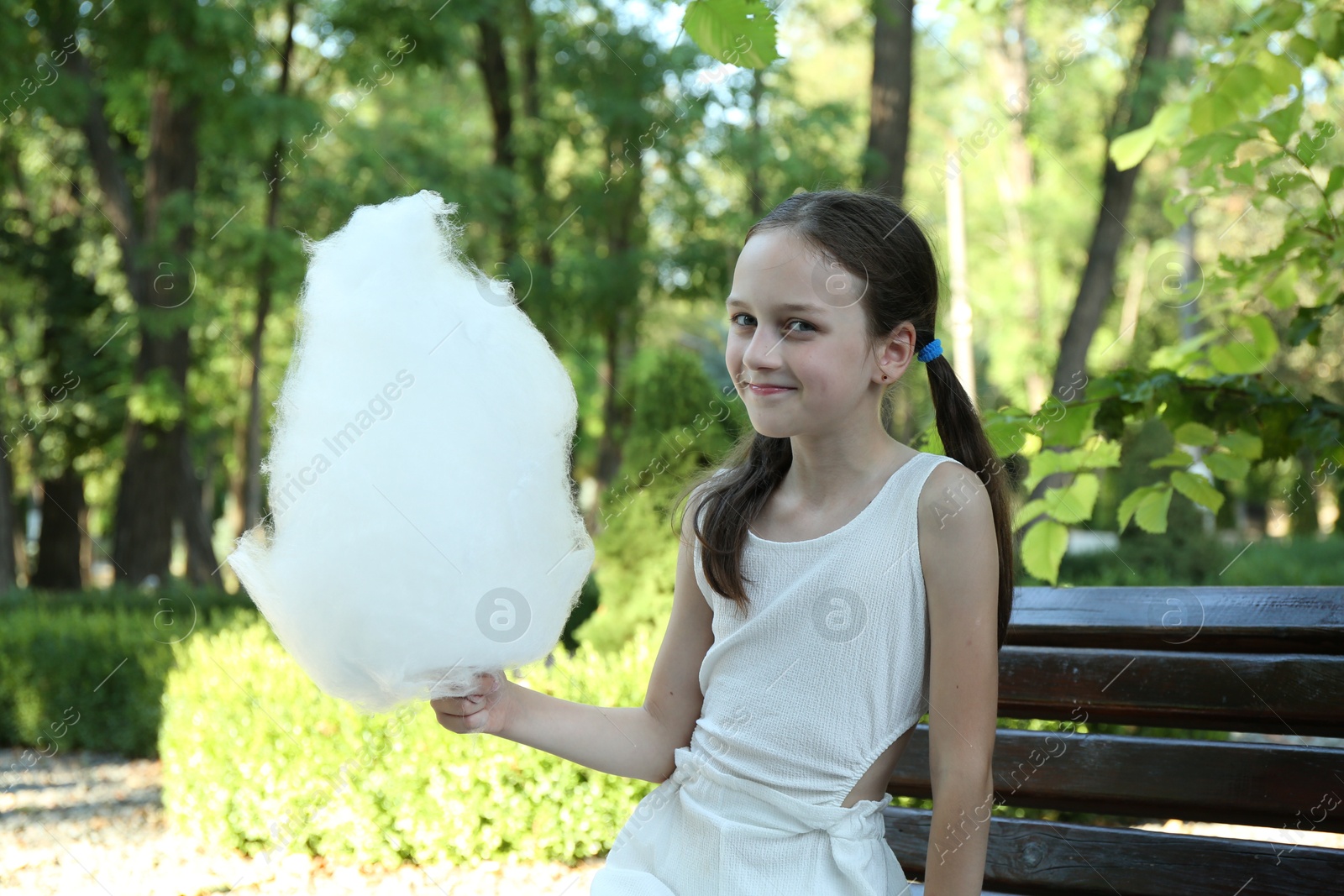 Photo of Portrait of little girl with sweet cotton candy on bench in park