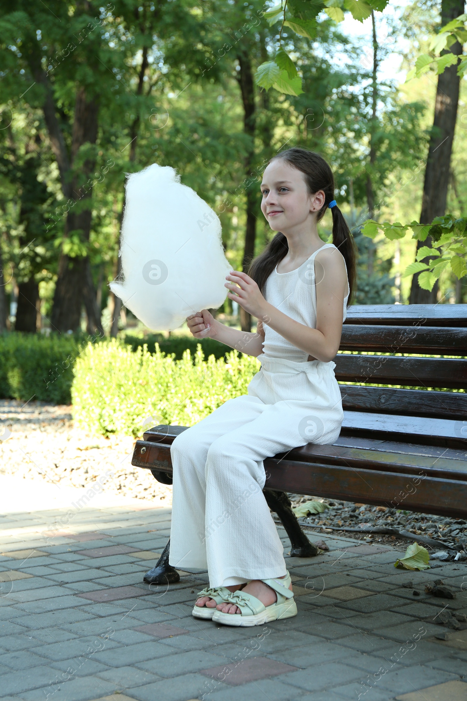 Photo of Little girl with sweet cotton candy on bench in park