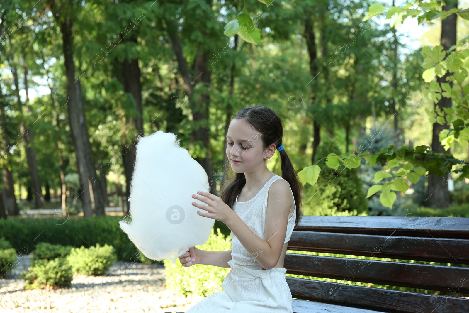 Photo of Little girl eating sweet cotton candy on bench in park