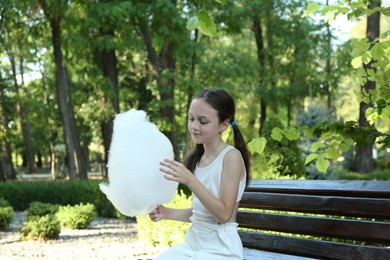 Photo of Little girl eating sweet cotton candy on bench in park