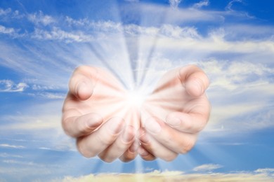 Woman with holy light in hands against sky, closeup