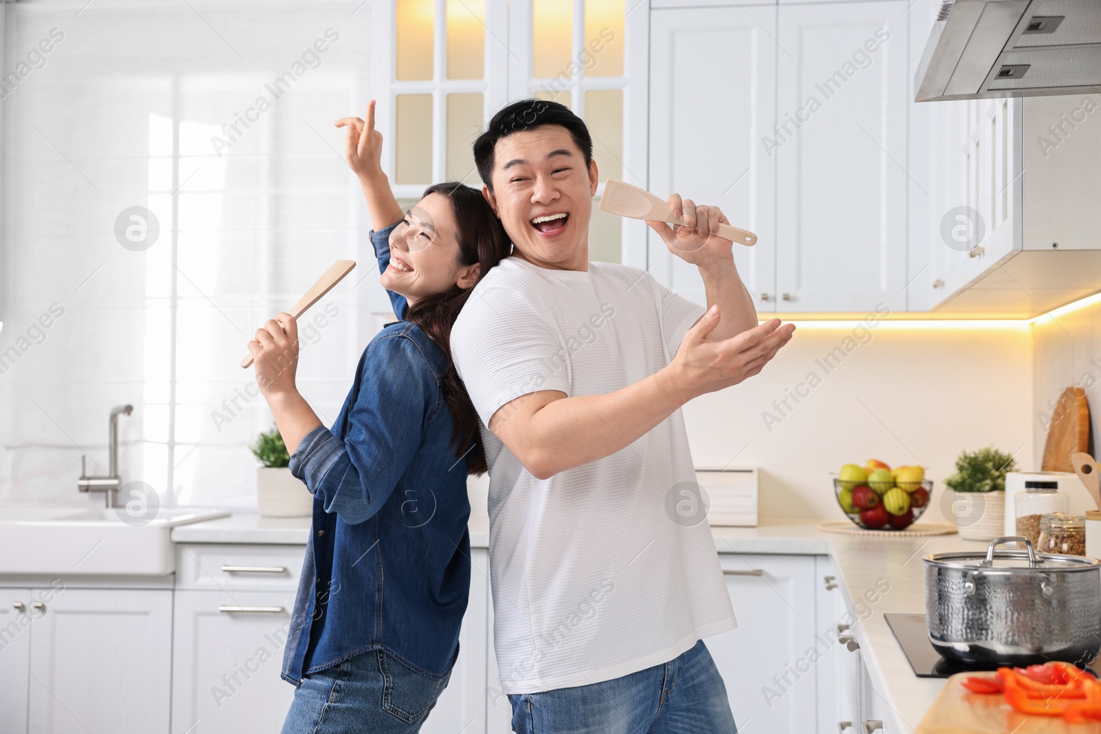 Photo of Happy lovely couple singing together while cooking in kitchen