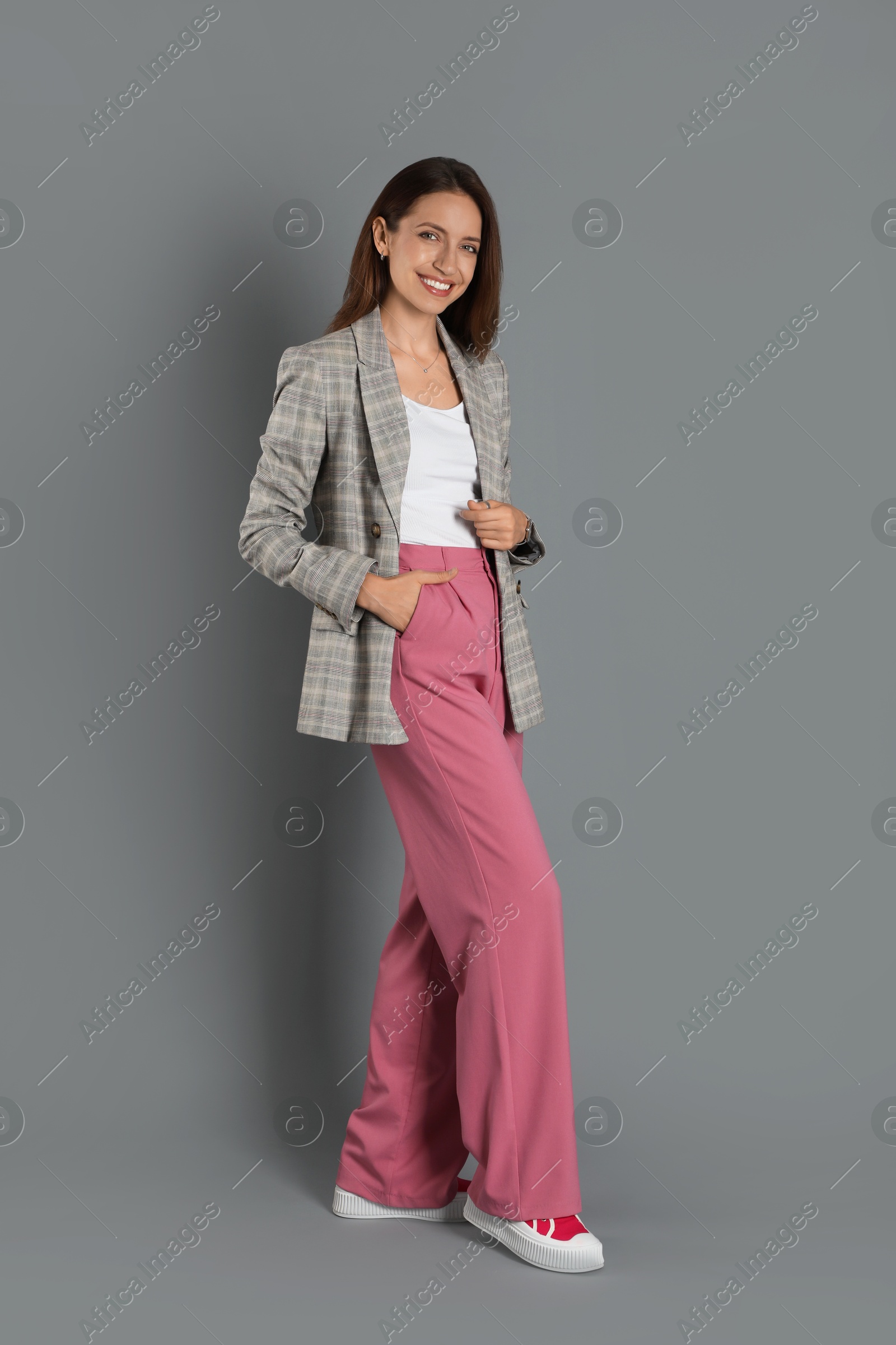 Photo of Beautiful woman in stylish jacket and pink pants on grey background