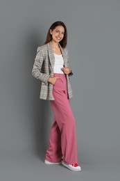 Beautiful woman in stylish jacket and pink pants on grey background