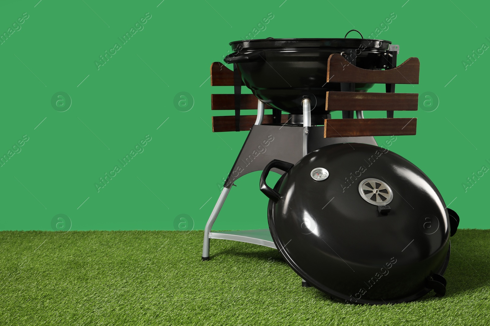 Photo of One black barbeque grill on grass against green background. Space for text