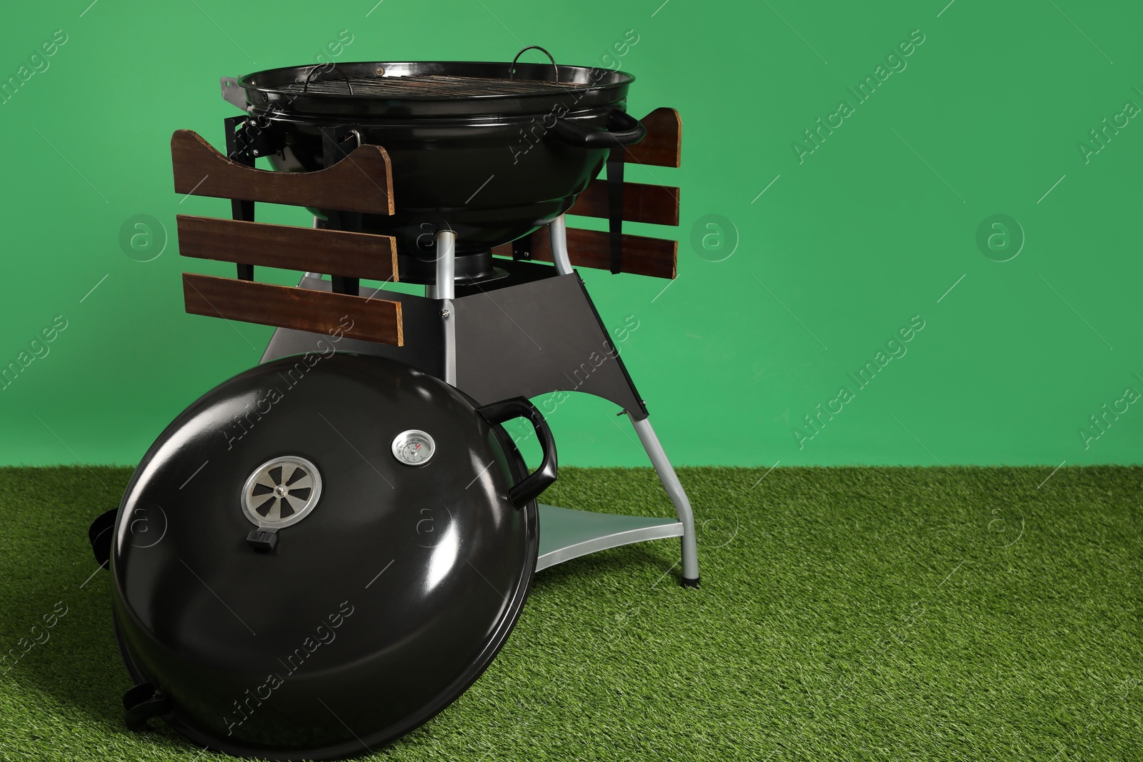 Photo of One black barbeque grill on grass against green background. Space for text