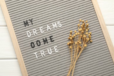 Letter board with phrase My Dreams Come True and dry plants on white wooden table, top view