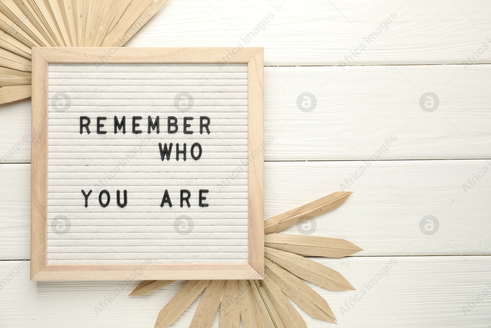 Photo of Letter board with phrase Remember Who You Are and decor elements on white wooden table, flat lay. Space for text