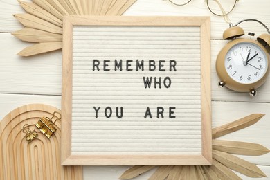 Flat lay composition of letter board with phrase Remember Who You Are on white wooden table