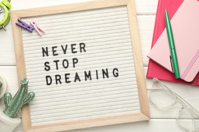 Letter board with phrase Never Stop Dreaming, glasses and stationery on white wooden table, flat lay