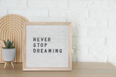 Photo of Letter board with phrase Never Stop Dreaming and plant on wooden table near white brick wall