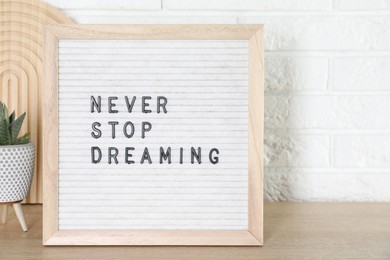 Photo of Letter board with phrase Never Stop Dreaming and plant on wooden table near white brick wall