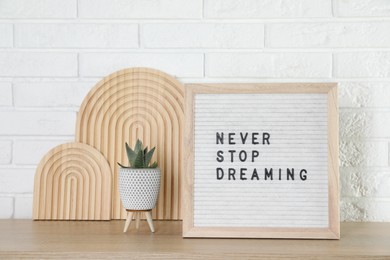 Photo of Letter board with phrase Never Stop Dreaming and plant on wooden table near white brick wall