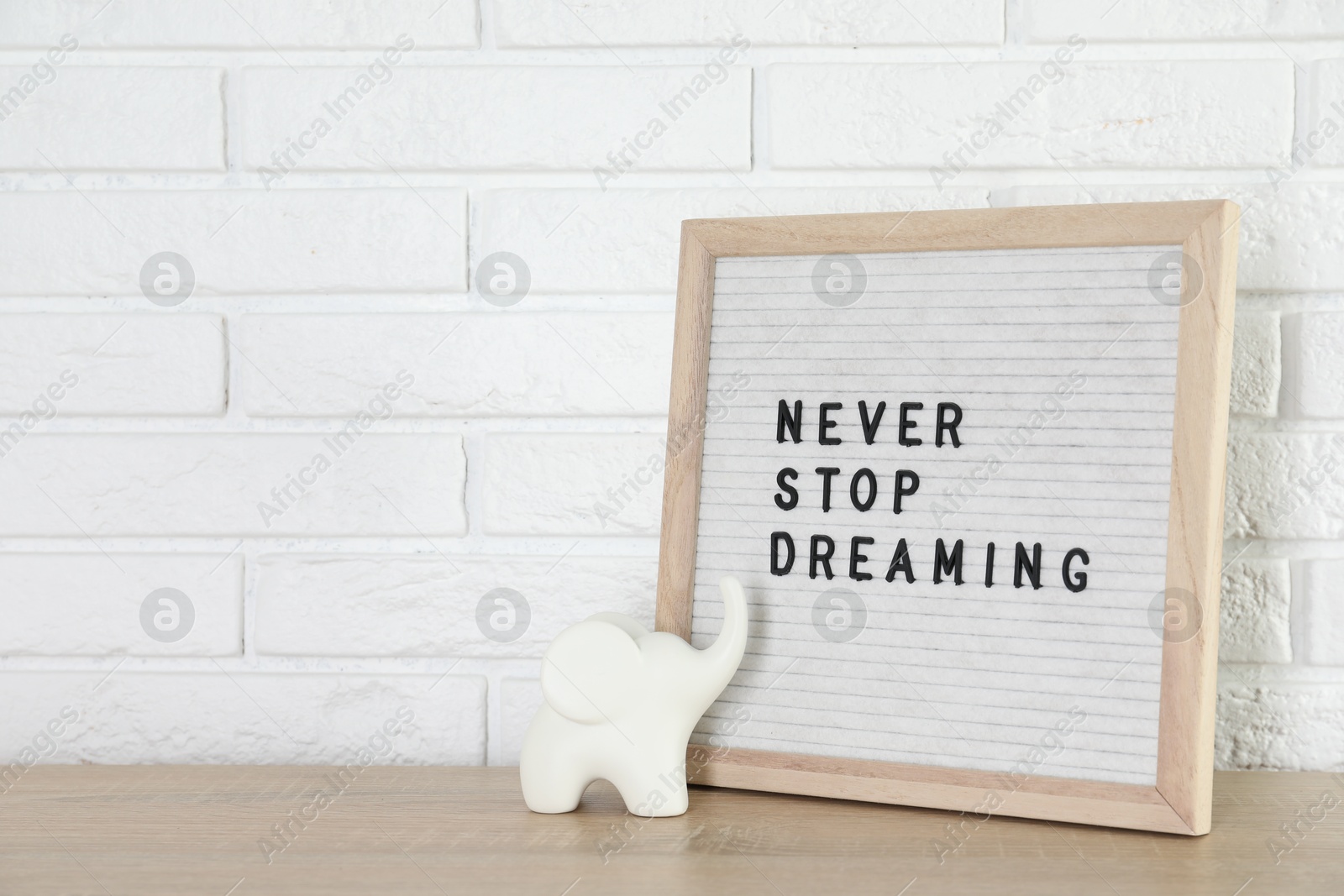 Photo of Letter board with phrase Never Stop Dreaming and elephant figure on wooden table near white brick wall, space for text