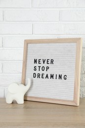 Photo of Letter board with phrase Never Stop Dreaming and elephant figure on wooden table near white brick wall