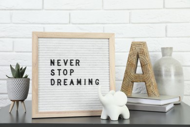 Photo of Letter board with phrase Never Stop Dreaming, plant, books and decor elements on grey table near white brick wall