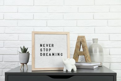 Letter board with phrase Never Stop Dreaming, plant, books and decor elements on grey side table near white brick wall