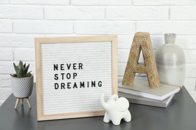 Photo of Letter board with phrase Never Stop Dreaming, plant, books and decor elements on grey table near white brick wall