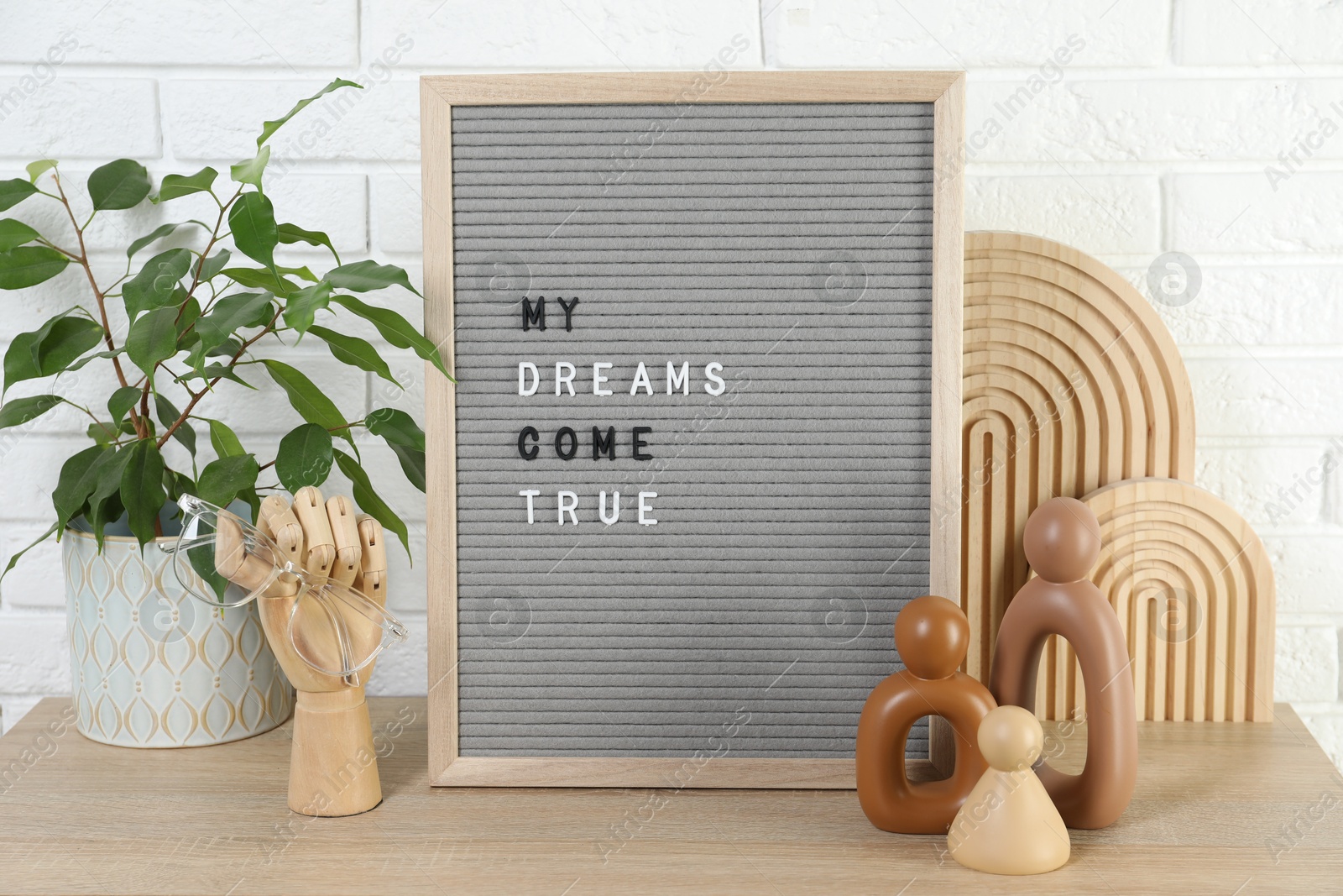 Photo of Letter board with phrase My Dreams Come True, plant and decor elements on wooden table near white brick wall