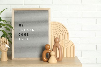 Photo of Letter board with phrase My Dreams Come True, plant and decor elements on wooden table near white brick wall