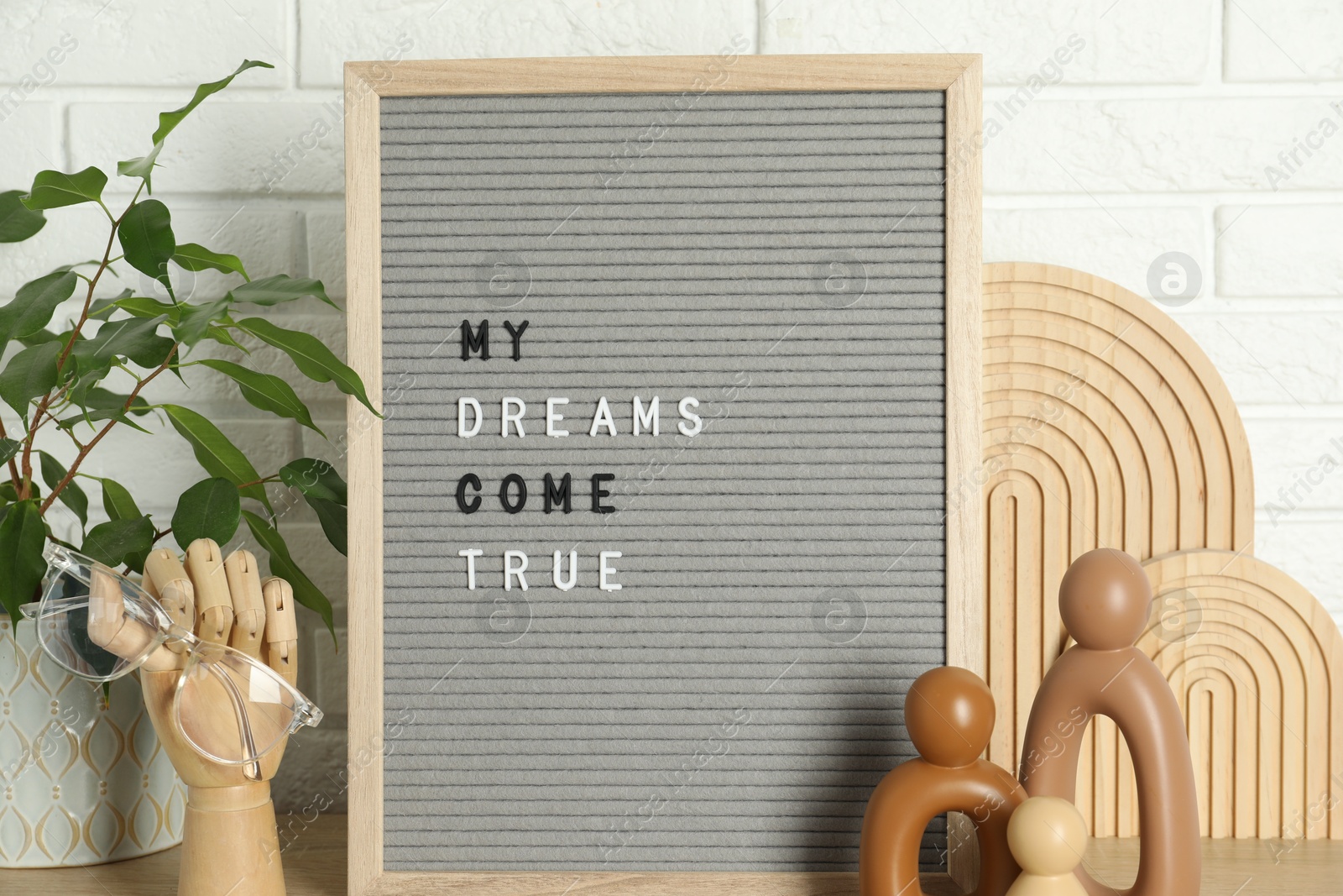 Photo of Letter board with phrase My Dreams Come True, plant and decor elements on wooden table near white brick wall