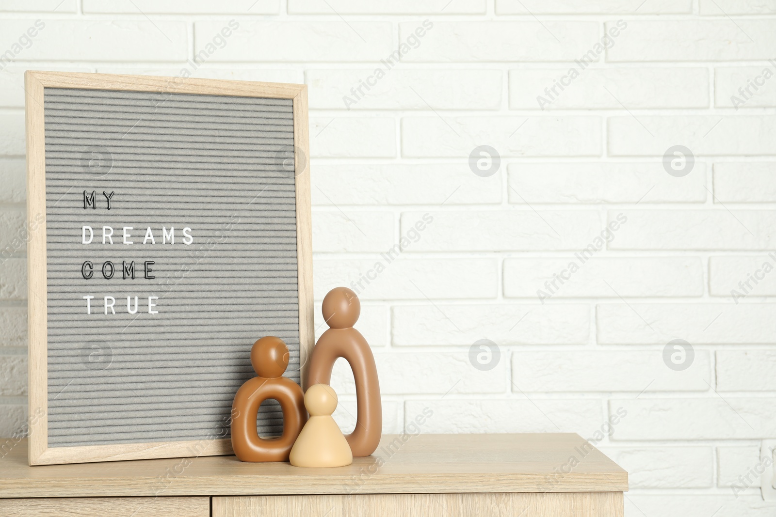 Photo of Letter board with phrase My Dreams Come True and decor elements on wooden side table near white brick wall, space for text