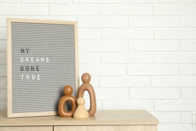 Photo of Letter board with phrase My Dreams Come True and decor elements on wooden side table near white brick wall, space for text