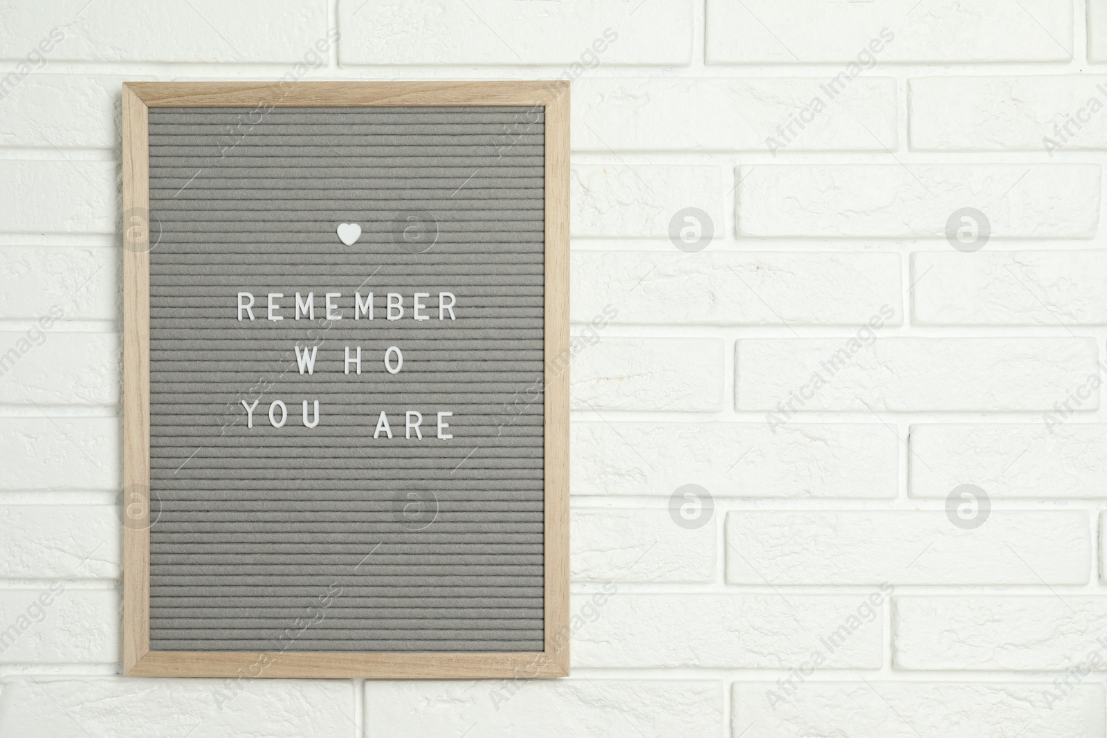 Photo of Letter board with phrase Remember Who You Are on white brick wall, space for text