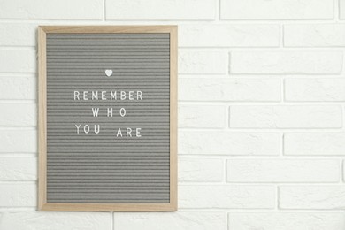 Photo of Letter board with phrase Remember Who You Are on white brick wall, space for text