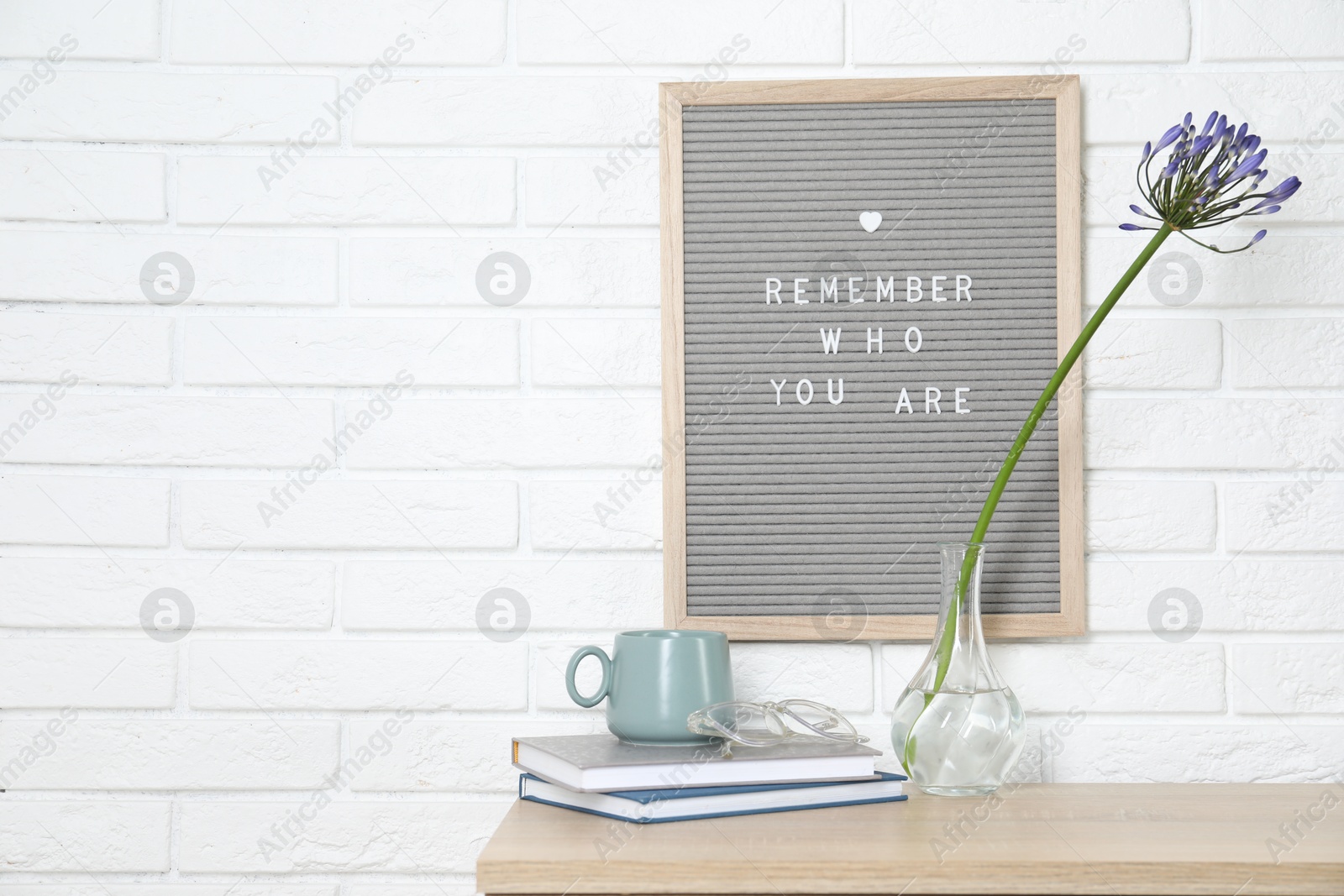 Photo of Letter board with phrase Remember Who You Are, books, cup and flower in vase on wooden table indoors, space for text